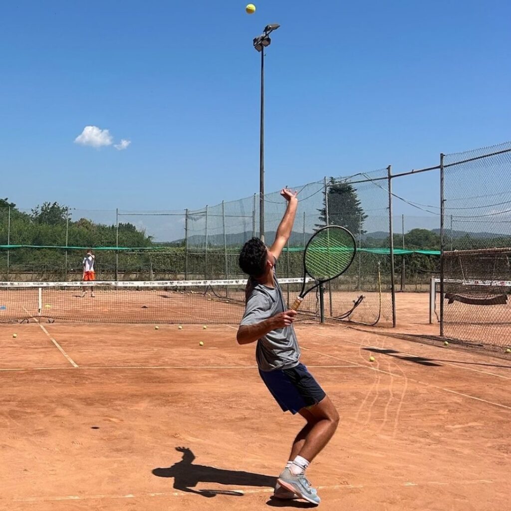 Junior tennis player serving on a red clay court in Spain